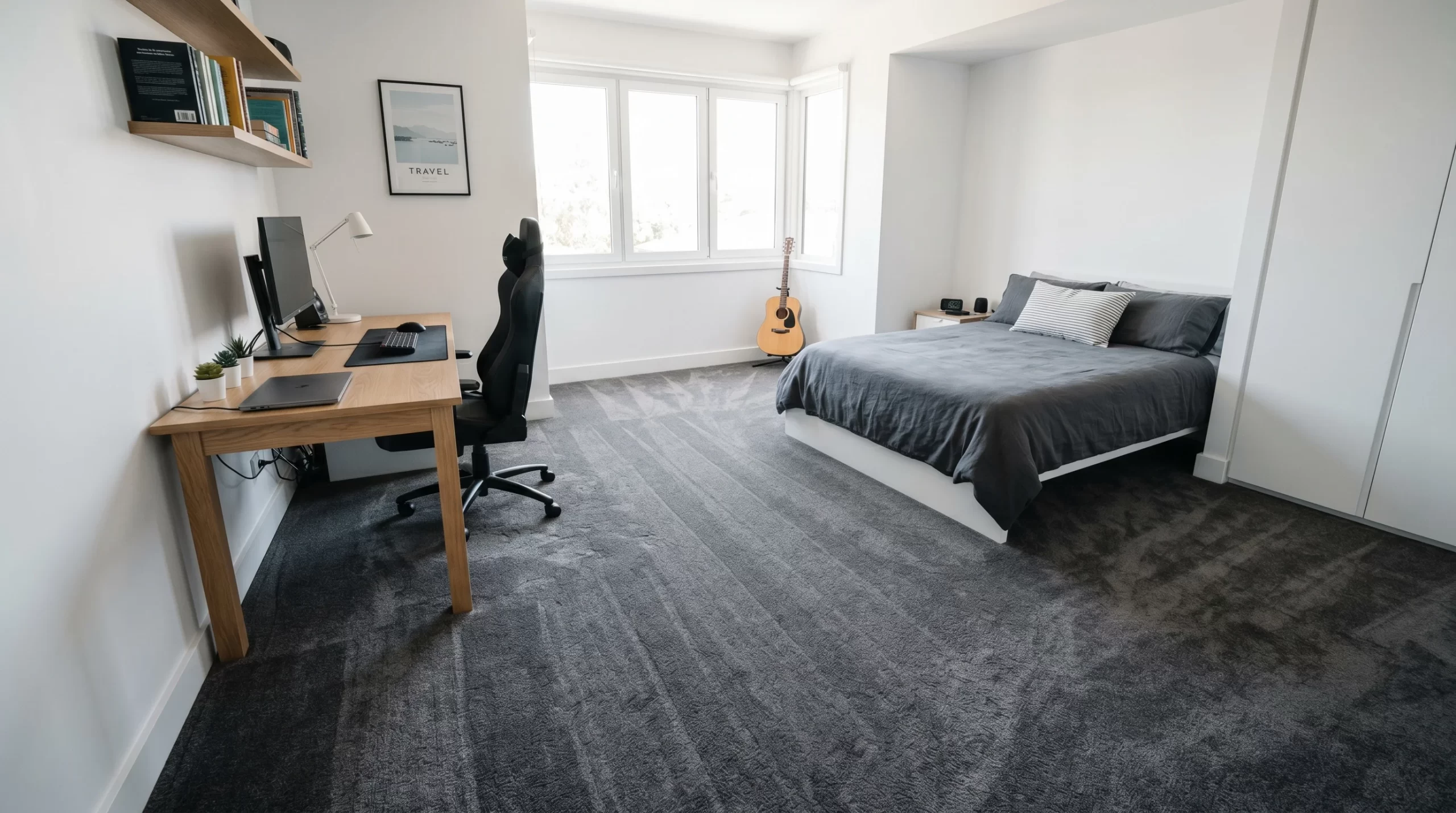 Clean bedroom and home office with dark carpet, desk, bed, and guitar